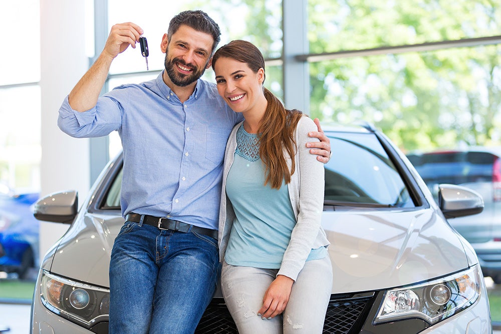 Happy couple smiling with car keys beside their new vehicle